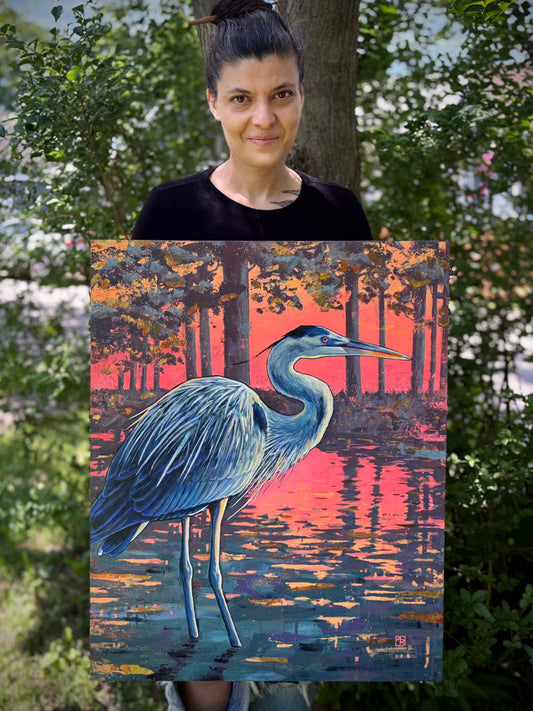 Person holding a painting of a heron at sunset with trees and water in the background.